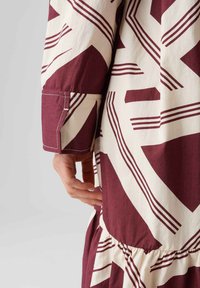 Abito a pois bordeaux e crema con forme geometriche, orlo arricciato e maniche con polsini abbottonati, realizzato in tessuto leggero.