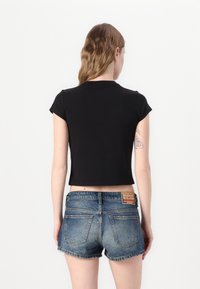 Černý krátký rukávový crop top v kombinaci s modrými džínovými šortkami. Top je přiléhavý a šortky mají roztrhaný lem a zadní kapsy.