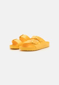 Sandales en caoutchouc jaunes avec deux boucles réglables, design ouvert à l'avant, semelle intérieure texturée et une semelle épaisse à rainures pour une meilleure traction.
