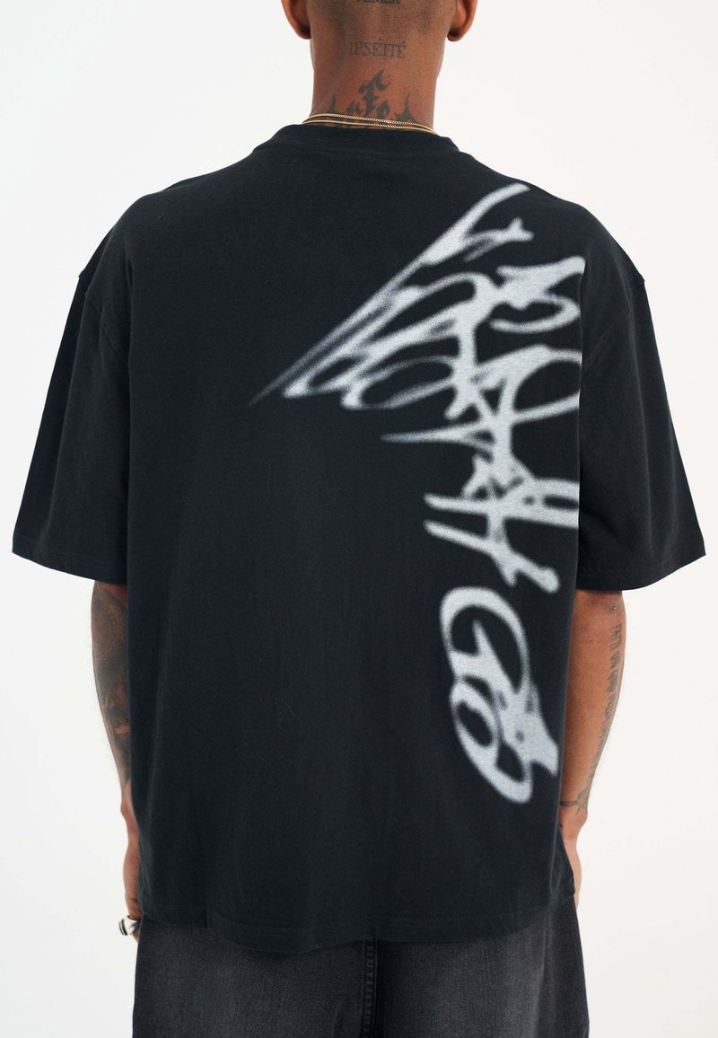 Černé oversized tričko s krátkým rukávem s bílým textem ve stylu graffiti na zádech. Měkká tkanina; uvolněný střih.
