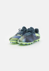 Botas de fútbol con parte superior azul oscuro, acentos en verde neón y diseños estampados. Presentan una superficie texturizada y tacos multicolores.