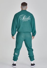 Sudadera en azul verdoso y joggers a juego con un corte relajado. Gran logo blanco en la parte posterior de la sudadera; puños y tobillos acanalados.