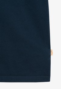 Tissu tricoté bleu foncé avec une petite étiquette beige sur le bord droit portant un texte orange indiquant "BLKYS."