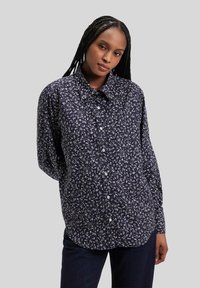 Chemise bleu marine à boutons avec motif floral blanc, manches longues et col classique. Tissu en coton doux avec une coupe décontractée.