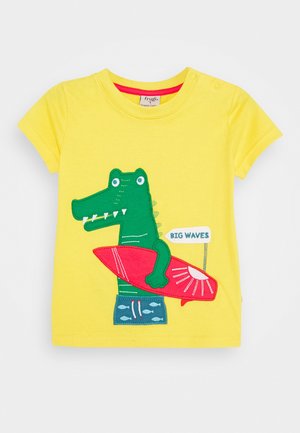 Geel peutershirt met een groene krokodil die een rode surfplank vasthoudt en een bord met de tekst "BIG WAVES".