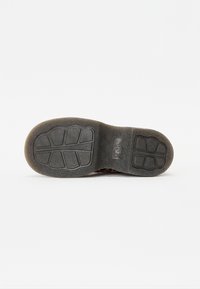Suela de zapato de goma negra con patrones de tracción texturizados, que presenta un borde liso y una impresión de logo. Diseño de puntera redondeada para mayor comodidad.