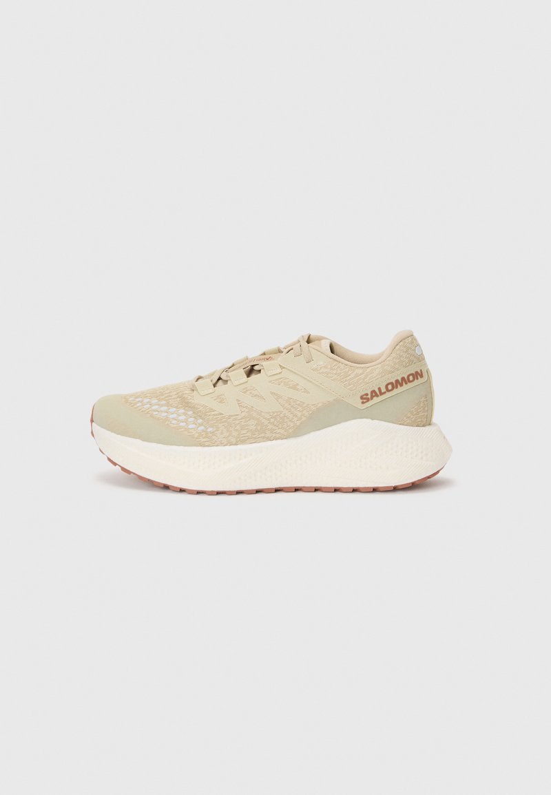 Beige løbesko med en tekstureret mesh-overdel, snørelukning, polstret krave og hvid mellemsål med et mønstret ydersål.