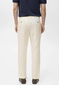 Pantalones de lino color crema con un corte recto, que presentan dos bolsillos traseros y botones marrones. Llevados con zapatos oscuros, vistos desde atrás.