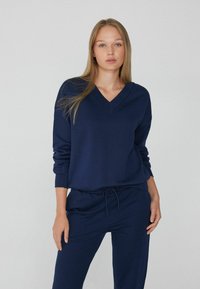 Sudadera de cuello en V azul marino con mangas largas, que presenta un ajuste relajado y puños acanalados, combinada con pantalones jogger con cordón a juego.