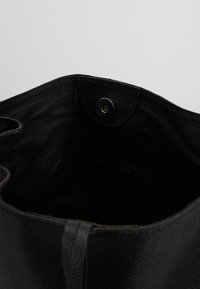 Svart läder tote-väska med en texturerad yta, med ett svart inre och en tryckknappsöppning högst upp. Inga ytterligare fack synliga.