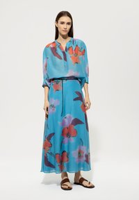 Ein fließendes, türkisfarbenes Kleid mit floralem Muster in Rottönen und Violett, das einen entspannten Schnitt, lange Ärmel und eine taillierte Taille aufweist.