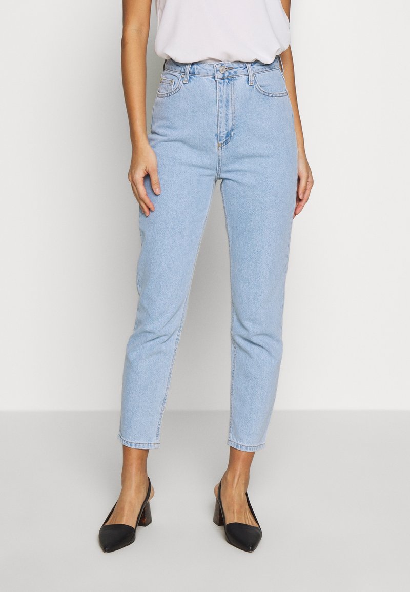 Jeans de cintura alta de color azul claro con un corte recto, sutiles desgastes en la parte frontal y bolsillos cosidos. Combinados con tacones negros de punta afilada.
