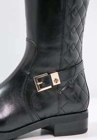 Bottes mi-mollet en cuir noir avec coutures matelassées, une boucle carrée dorée sur la bride de la cheville et un petit talon carré.