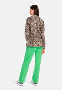 Leopard print long-sleeve top, green sweatpants, and matching leopard print shoes. The outfit showcases contrasting patterns and vibrant colors.