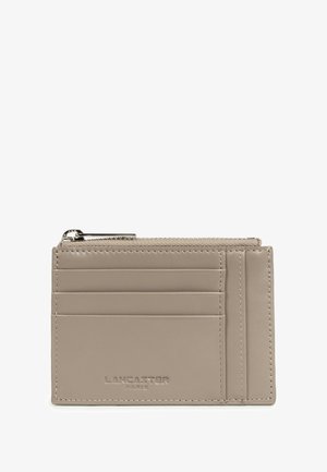 Taupe lederen kaart houder met zes kaartsleuven, een ritsvak voor munten bovenop en het geëmbosseerde logo "LANCASTER PARIS" aan de voorkant.