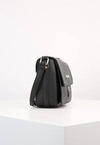 Svart läderaxelväska med vikbar lucka, guldfärgad hårdvara och texturerad yta, med en avtagbar rem för mångsidig användning.