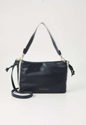 Námořnická kožená kabelka s hladkou texturou, zdobená bílým zipem, zlatými doplňky a nastavitelným popruhem.