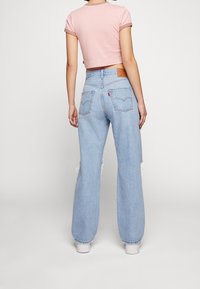 Maglietta cropped rosa chiaro con colletto a righe, abbinata a jeans leggeri azzurri a vita alta e un fit ampio con orlo strappato e tasche a toppa.