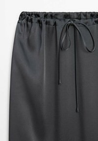 Jupe en satin noir avec une taille élastiquée et un lien assorti, présentant une texture lisse et une coupe fluide.