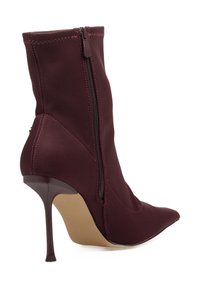 Bota burdeos con punta afilada y tacón alto de aguja. Fabricada en tela suave, presenta un cierre lateral de cremallera y costuras decorativas.