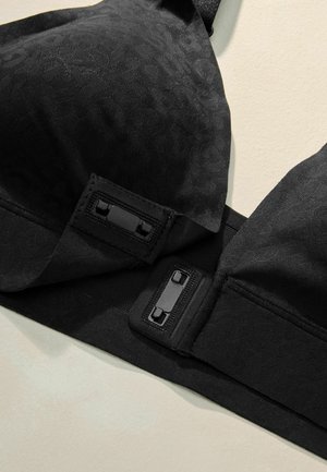 Černá podprsenka z texturované látky s jemným vzorem, vybavená nastavitelnými ramínky a černým zapínáním.