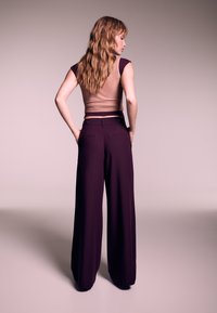 Top marrone aderente a coste abbinato a pantaloni viola scuro a gamba larga. I pantaloni presentano tasche posteriori e dettagli con bottoni.