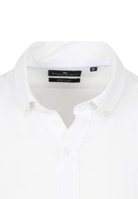 Witte linnen shirt met een button-down kraag, korte mouwen en een etiket dat maat medium en samenstelling van het materiaal aangeeft.