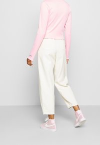 Rosa långärmad topp med vågig nederkant, vita vida byxor och rosa högskaftade sneakers. Slät tyg och avslappnad passform genomgående.