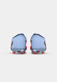Des chaussures de sport bleues avec des accents rouges, présentant un dessus en synthétique lisse, un talon arrondi et une semelle transparente avec des pointes rouges.