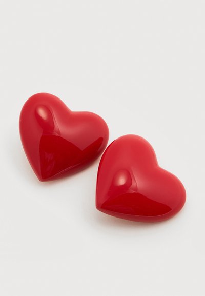 Deux objets brillants en forme de cœur rouge placés près l'un de l'autre sur un fond gris clair, reflétant une lumière douce.