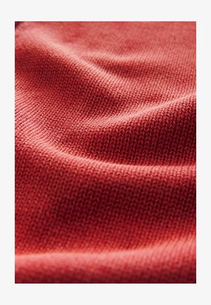 Blødt, tekstureret strikket stof i en varm, afdæmpet rød nuance med et nærbillede af sammenvævede mønstre og bløde folder.