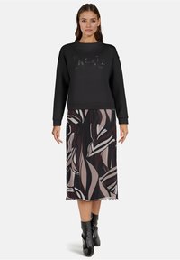 Zwarte sweatshirt met gestructureerde "Create" opdruk, gecombineerd met een midi-jurk met abstracte bladzijdenpatronen in donkere en lichte tinten. Zwarte enkellaarsjes.