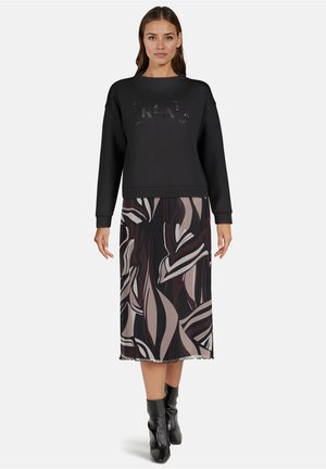 Czarna bluza z teksturowanym napisem "Create", zestawiona z midi spódnicą z abstrakcyjnym wzorem liści w ciemnych i jasnych odcieniach. Czarne botki za kostkę.