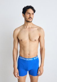 Boxer in blu con elastico bianco in vita che presenta il testo "BJÖRN BORG." Tessuto morbido, design aderente e lunghezza a metà coscia.