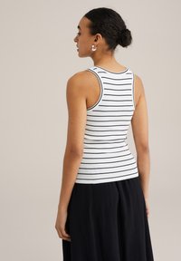 Canotta bianca a righe orizzontali blu navy, con scollatura rotonda e forma aderente. Abbinata a una gonna lunga nera.