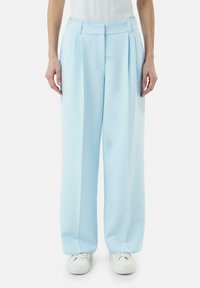 Jasnoniebieskie spodnie o szerokich nogawkach wykonane z miękkiego materiału, z plisami z przodu i dopasowaną talią, zestawione z białymi trampkami.