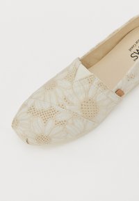 Bottines en toile beige à enfiler avec broderies florales, dotées d'un bout arrondi et d'une texture subtile. Comprend une petite étiquette de marque près de la semelle.