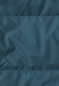 Turquoise pufferjack in stof met een gladde, glanzende textuur met zichtbare stiklijnen en een subtiele glans. Geen opvallende patronen of hardware.