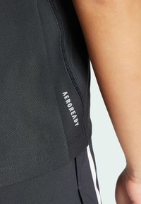 Svart atletisk t-shirt med ett texturerat, ventilerande tyg. Har "AEROREADY"-märkning på sidan och sömnadsdetaljer nära fållen.