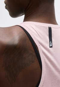 Κοντινό πλάνο στο πάνω μέρος της πλάτης και τον ώμο ενός ατόμου που φοράει ένα ανοιχτό ροζ αμάνικο με το λογότυπο The North Face στο πίσω μέρος του λαιμού.