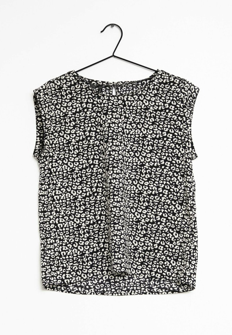 Blouse noire sans manches avec motif léopard blanc irrégulier suspendue sur un cintre en fil noir sur fond blanc.