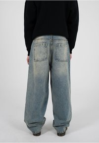 Jeans de denim de lavado claro y pierna ancha con un acabado desgastado. Cuenta con dos bolsillos traseros y una cintura alta, diseñados para un ajuste holgado.