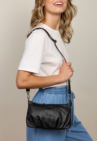 Zwarte leren handtas met een zacht, geplooid ontwerp, korte schouderriem en een ritsluiting. Geweven afwerking en subtiel zichtbaar merkembleem.