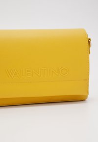 Gul läderväska med en texturerad yta. Har det präglade "VALENTINO"-loggan. Rektangulär form med dragkedjestängning och subtila sömnadsdetaljer.