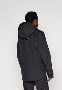 Czarna wodoodporna kurtka z kapturem, matowa tekstura, luźny krój, z rzepami na mankietach i subtelnym logo na plecach.