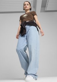 Lysblå vide jeans med en løs pasform, parret med en brun grafisk t-shirt og en sort hoodie knyttet om livet. Hvide sneakers.