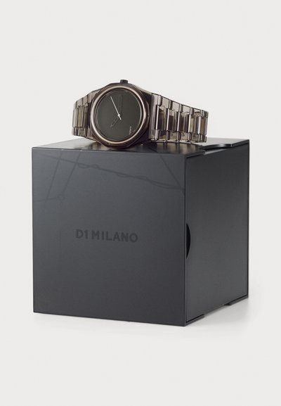 D1 Milano watch with a round black dial, silver-tone metallic band, polished finish, displayed on a black box with embossed logo.
