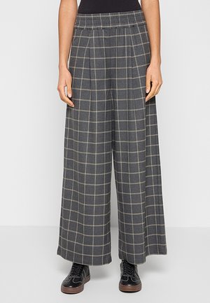 Grijze wijde broek met beige ruitpatroon, elastische tailleband, gedragen met zwarte sneakers en een zwart shirt, getoond van taille tot voeten.