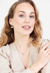 Gouden sieraden met een oogvormige hanger aan een delicaat ketting, aangevuld met bijpassende oorbellen en een armband.