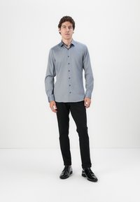 Cămașă albastră deschisă cu mâneci lungi, cu un buzunar la piept, asociată cu pantaloni negri slim-fit și pantofi negri lucioși. Design simplu.